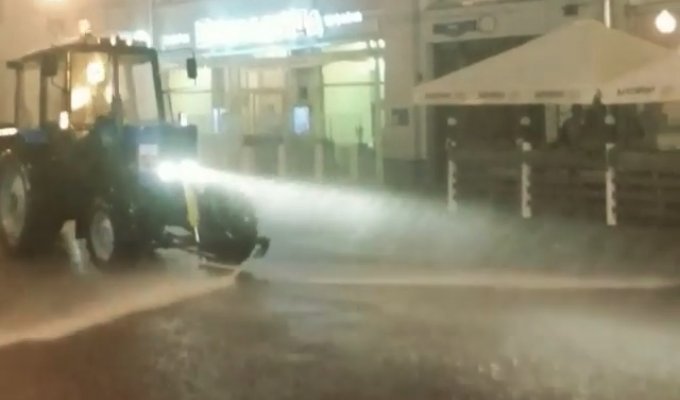 Трактор моет улицы Москвы во время дождя 