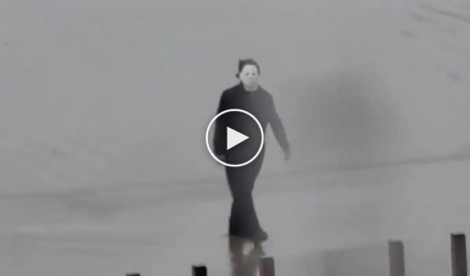 Человек в костюме Майкла Майерса, держа в руках нож, гуляет по улице и пугает местных жителей