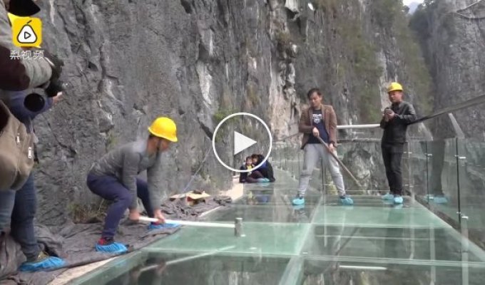 Робітники за допомогою кувалд випробовують на міцність новий скляний міст у горах Китаю.